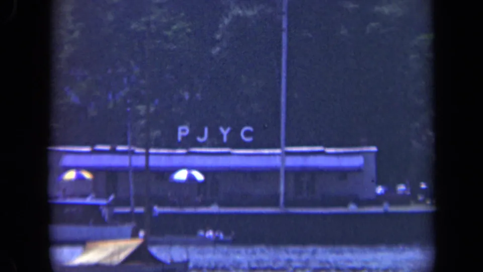 The PJYC-marked vessel remains centered against trees and dark water in this 1948 Long Island home-movie frame.