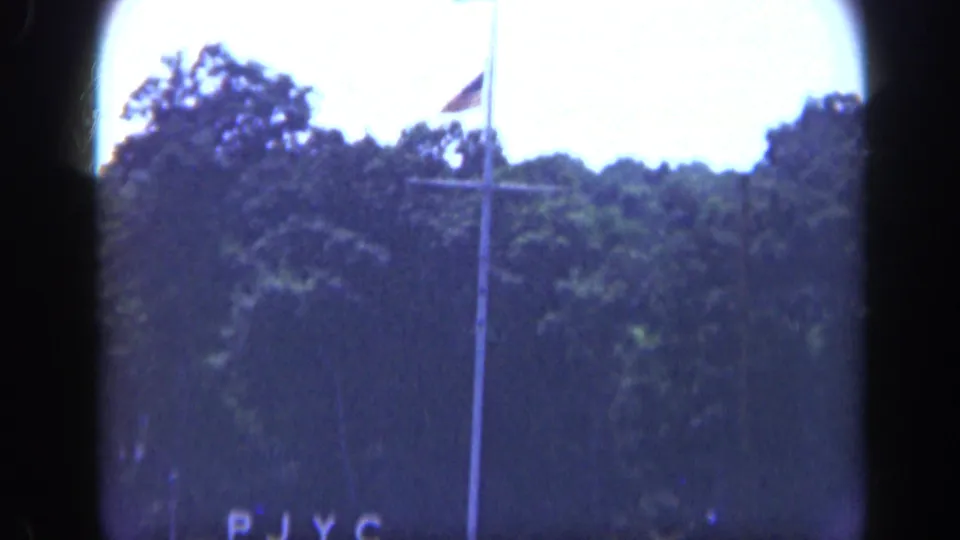 1948 Long Island waterfront view with a flagpole, partial PJYC lettering, trees, and soft 8mm framing.