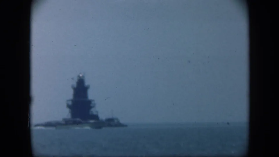 1948 Long Island footage holds on a distant naval-looking vessel or towered maritime structure against a pale sky.