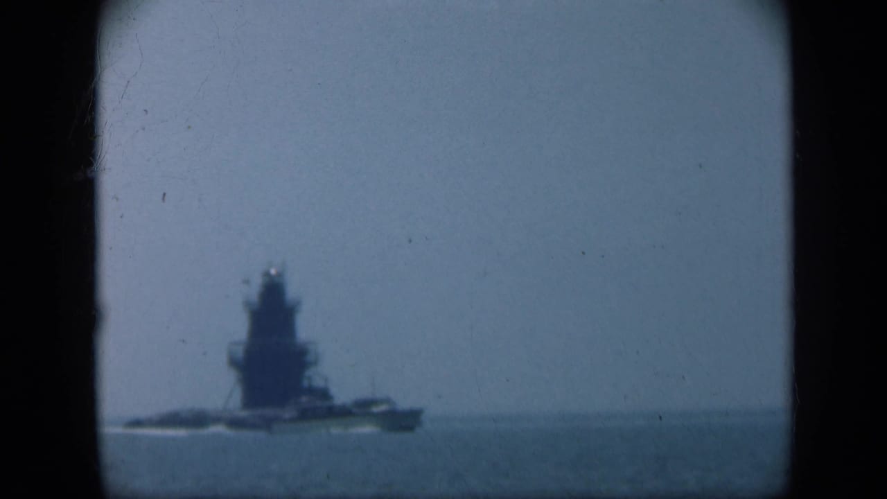 Distant naval ship on open water with a hazy horizon and dark 8mm frame edges.