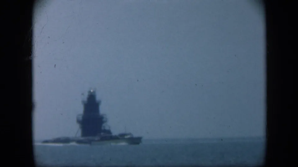 1948 Long Island 8mm frame showing a distant naval ship moving across open water under a hazy blue sky.