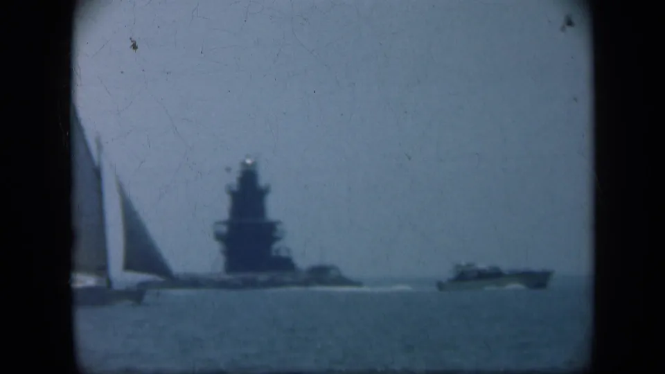 A sailboat crosses the foreground while a large naval ship remains beyond it in 1948 Long Island home-movie footage.