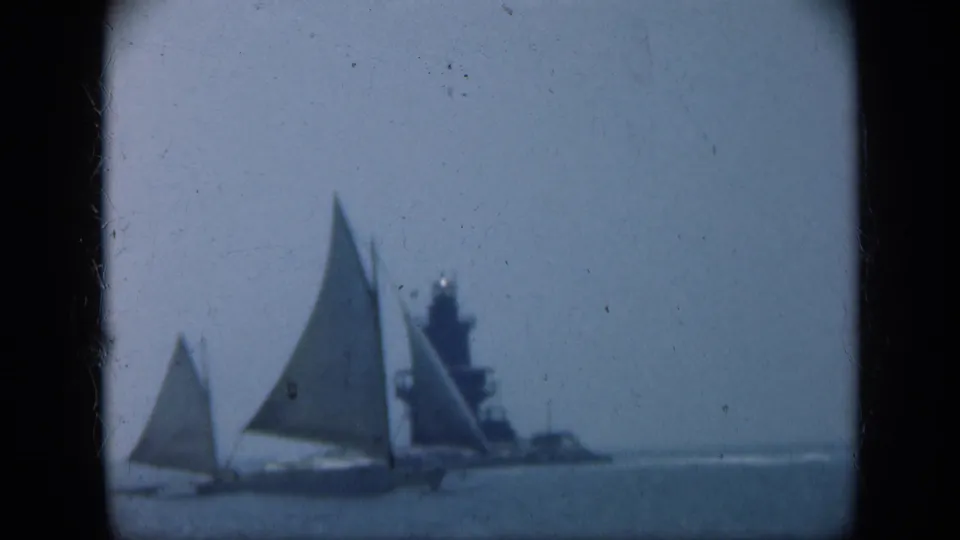 Two sailboats move across the foreground with a distant naval ship behind them in 1948 Long Island 8mm footage.