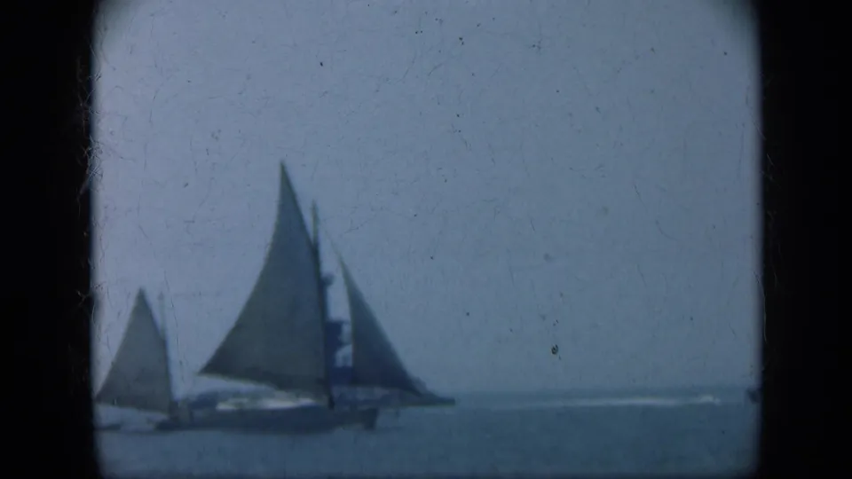 1948 Long Island 8mm frame showing two sailboats on open water with a distant lighthouse or tower under a hazy sky.