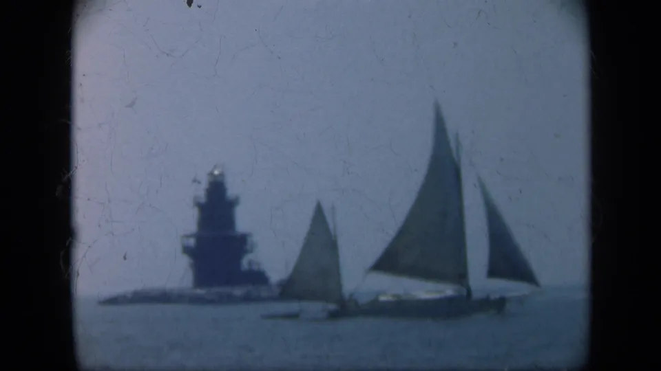 1948 Long Island 8mm still showing two sailboats under hazy light with a coastal lighthouse or tower rising in the background.