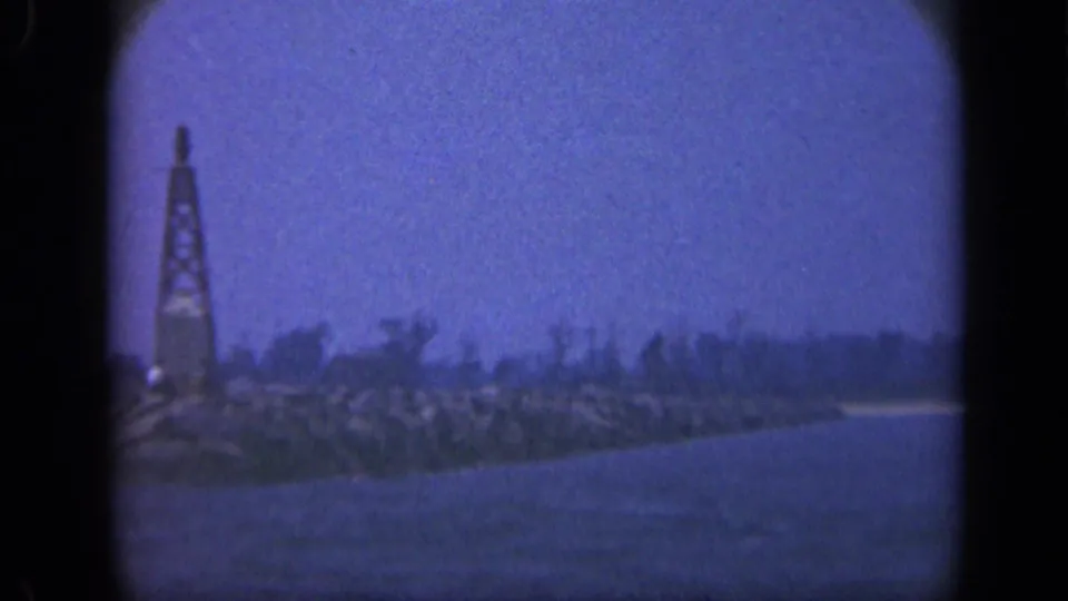 Closer 1948 Long Island shoreline view from the sea, with rocks, low trees, and a tall beacon-like or mast-like structure.
