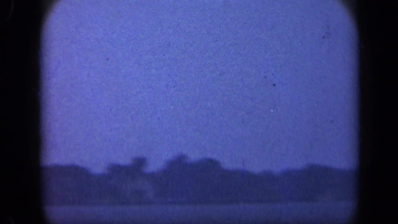 1948 Long Island 8mm frame showing calm water, a distant dark treeline, and a blue-purple sky through a soft home-movie scan.