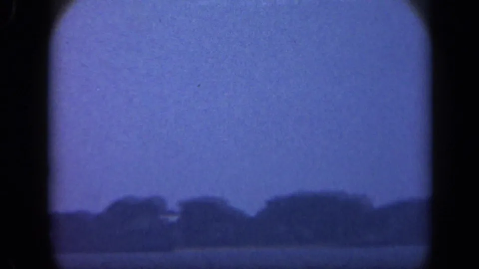 Blue-tinted 1948 Long Island home-movie frame with calm water in front of a distant treeline and faint shoreline shapes.