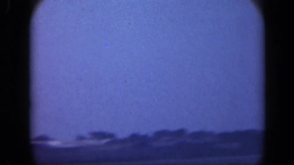 1948 Long Island 8mm view with a broad blue sky, water foreground, and a low dark shoreline passing near the lower frame.