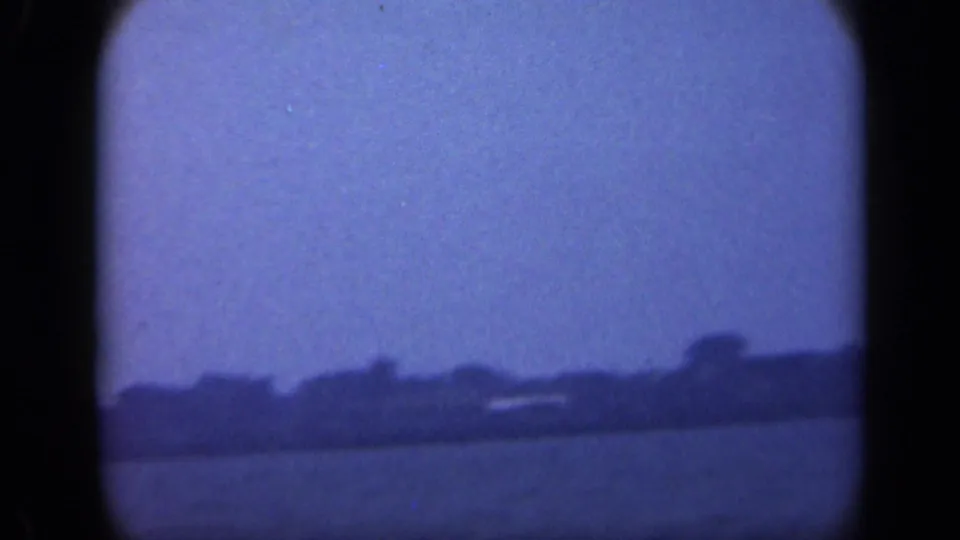 Final 1948 Long Island frame showing calm water, a dark treeline, and a faint light-toned shoreline structure under blue filtration.