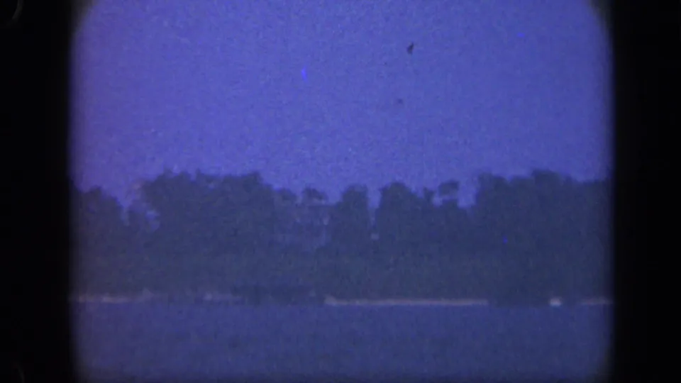 Final 8mm frame of the Long Island lakeside scene, with calm water and a tree-lined shore in soft focus.