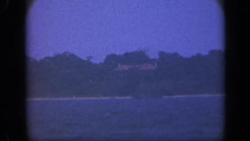 Soft 8mm view of Long Island bay water and a wooded shore with faint distant structures.
