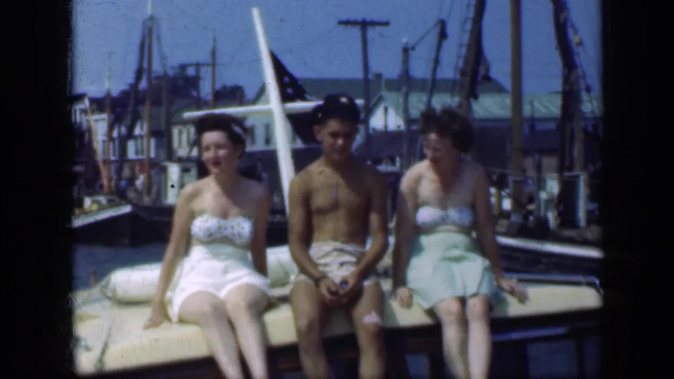 Three adults are seated on a small boat in Long Island, with the young man in a captain hat between two women at the marina.