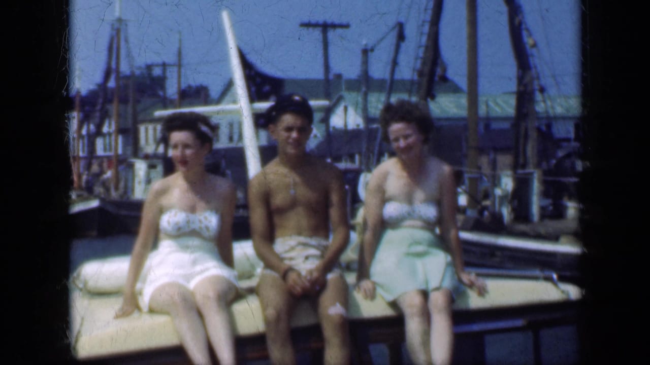 Two women and a man in swimwear sit on a boat bench in a harbor.