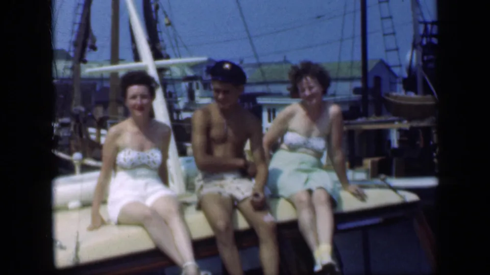 Three adults smile on a sunlit boat deck in a 1948 Long Island marina scene, with sailboat rigging and dock buildings visible behind them.