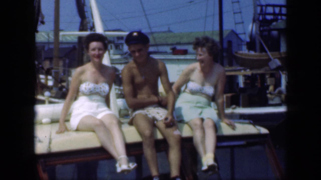 In 1948 Long Island home-movie footage, two women and a man sit on a moored sailboat with rigging and boats behind them.