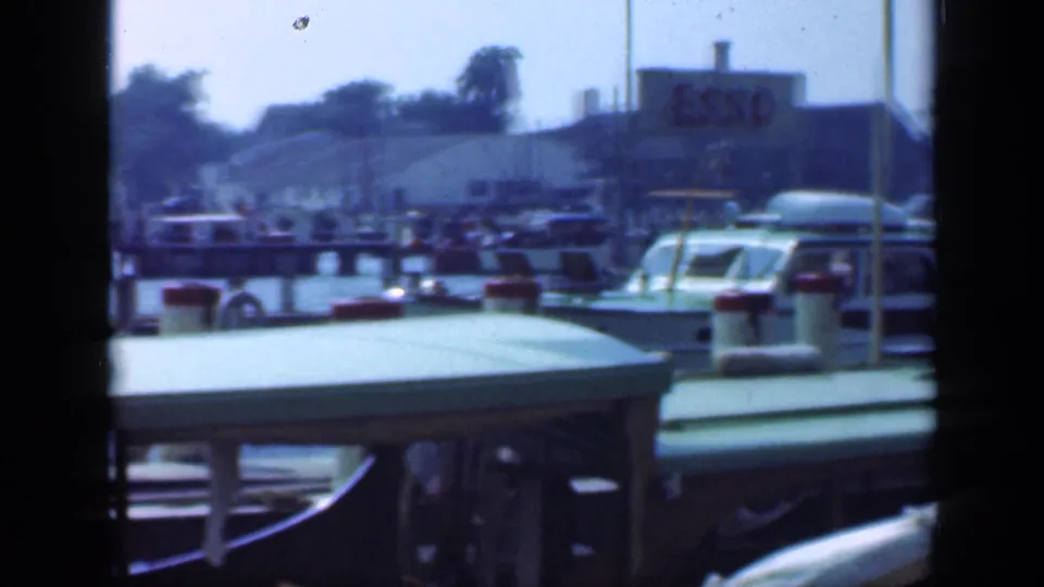 Long Island marina scene with docked boats, vertical poles, and an Esso sign on a shoreline building in the distance.