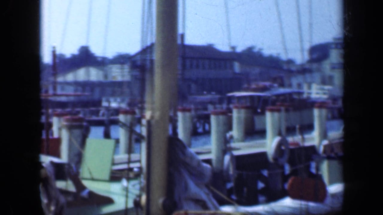 View through boat framing toward docked boats, pilings, and marina buildings.