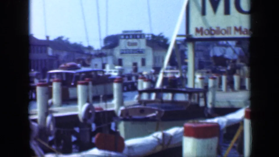 Long Island fuel dock with Mobilgas and marine fuel signage, red-topped pilings, boats, and marina structures visible.