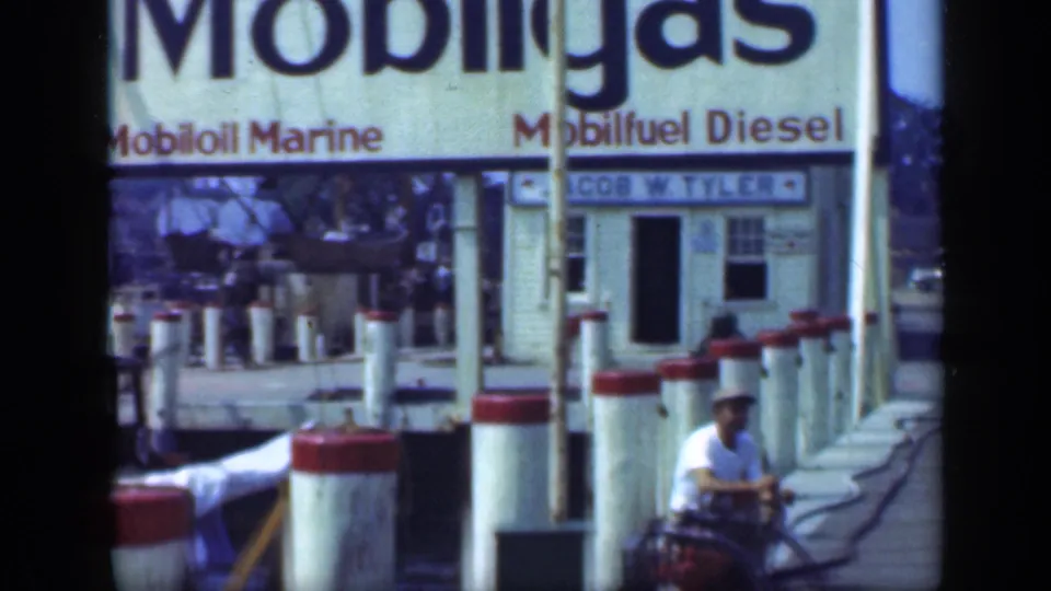 1948 Long Island dock scene with Mobilgas, Mobiloil Marine, and Mobilfuel Diesel signs, plus a man operating a small vehicle near the pilings.