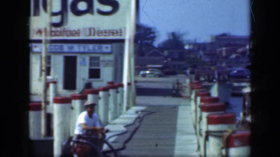 Long Island marina dock with red-topped pilings leading past a Mobilgas fuel building, with boats and waterfront structures beyond.