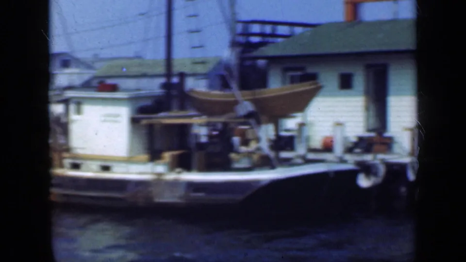 A cabin boat sits moored at a Long Island harbor in 1948, with dockside equipment, buildings, and rigging visible behind it.