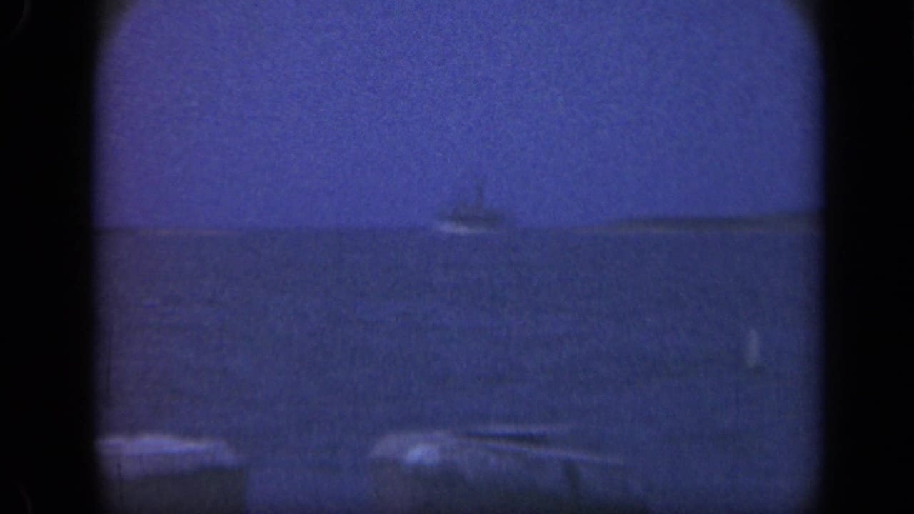 Blue-toned ocean horizon with a distant vessel and pier posts in the foreground.