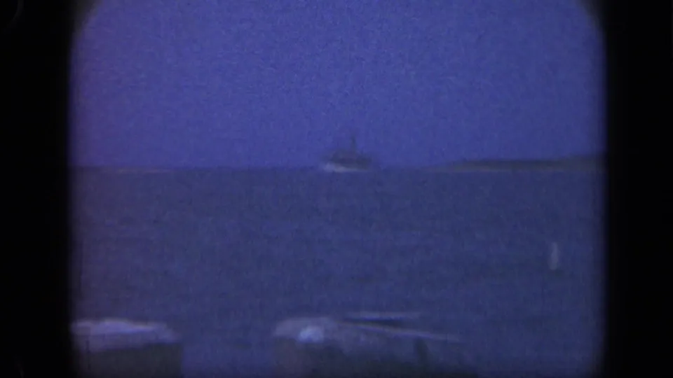1948 Long Island home-movie frame showing a distant vessel offshore beyond dark wooden pier posts in blue twilight light.