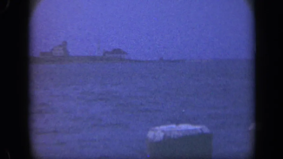 Late-1940s Long Island 8mm frame showing a distant vessel silhouette across the ocean, framed by a foreground pier post.