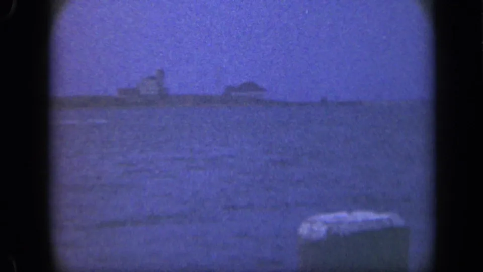 1948 Long Island home-movie frame showing a distant harbor edge across calm water with soft blue 8mm color.
