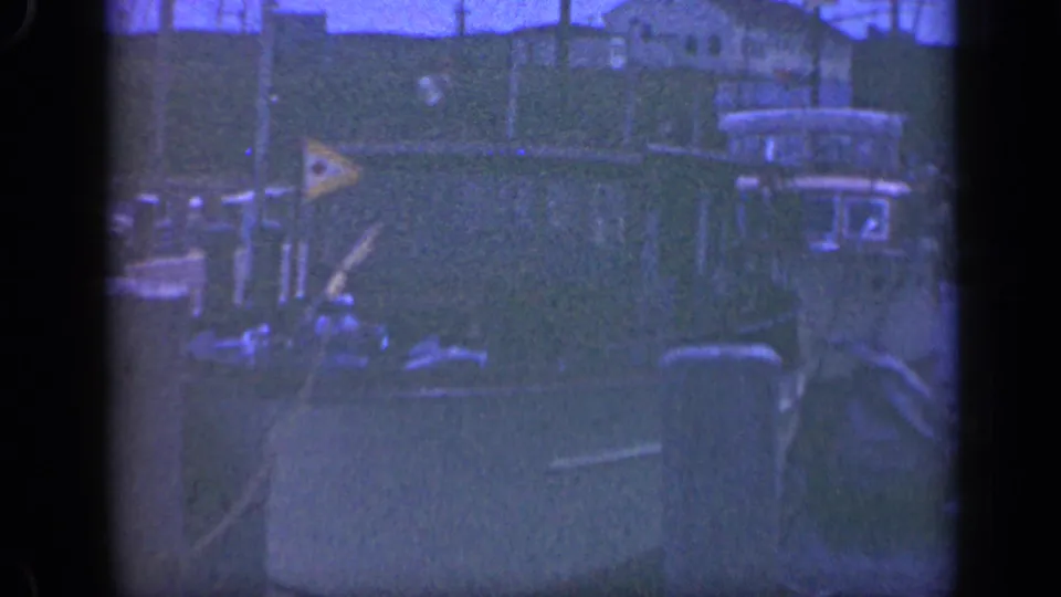 Small harbor view in Long Island, 1948, with moored boats, dock pilings, rigging, and houses behind the berth.