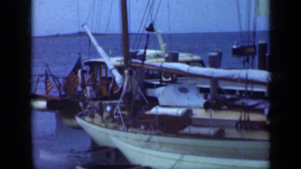 1948 Long Island frame of a white-hulled sailboat with wooden deck, rigging, small flag, and adults partly visible near the cabin.