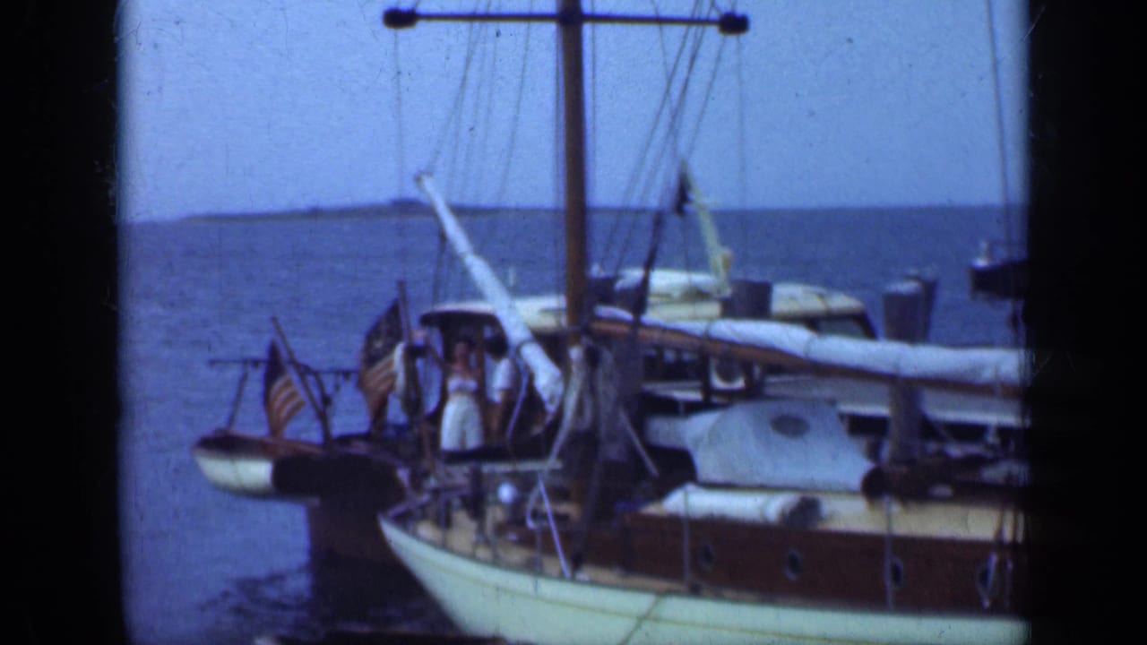 Wooden sailboats docked near a pier with flags and people on deck.