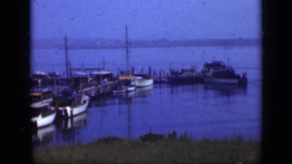 Long Island harbor footage shows small boats clustered around a pier, with tiny figures visible near the moorings.