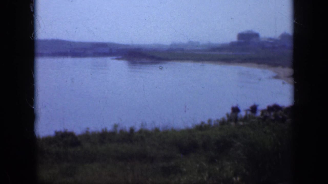 Still lake seen past a dark frame edge with grassy bank and distant low shoreline.