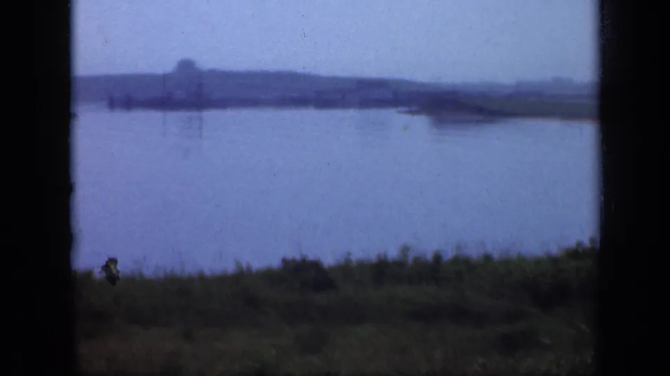 Soft 8mm view across a still Long Island lake toward a low, hazy shoreline under cloudy sky.