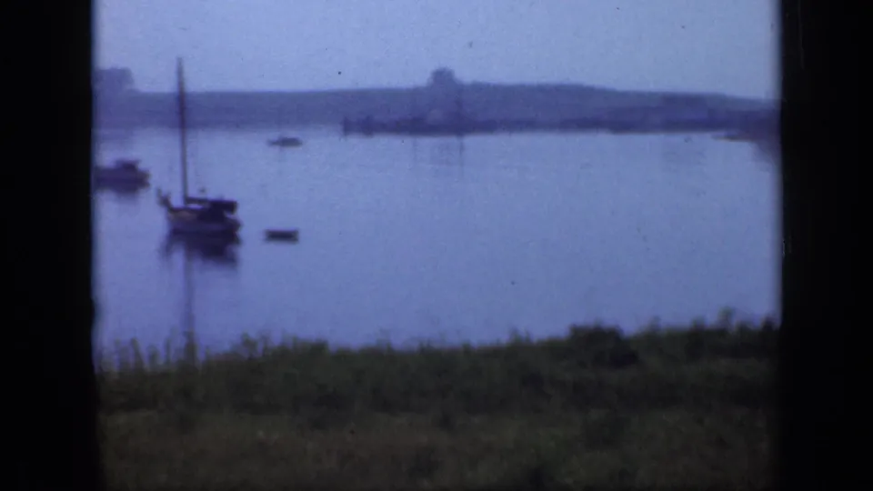 1948 Long Island lake view with small moored sailboats, faint reflections, grassy foreground, and distant shore.