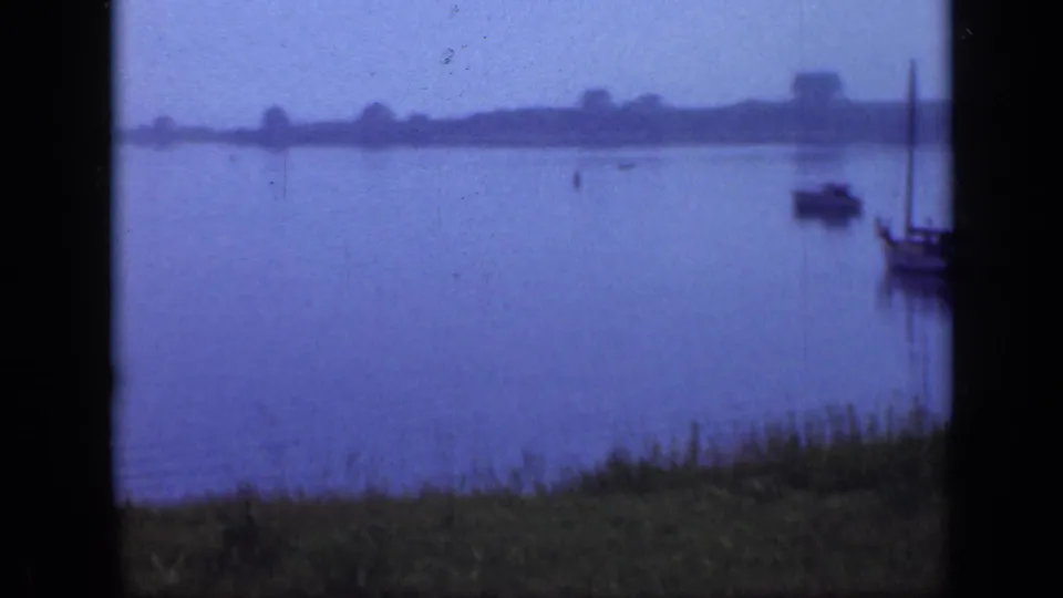 Soft 8mm view of Long Island waterfront boats under a hazy sky, with a grassy bank in the foreground.