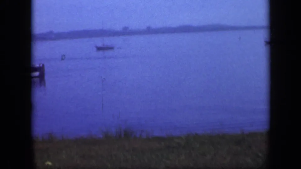 Blue-tinted 1948 Long Island waterfront view with anchored boats and a distant low shoreline across the bay.