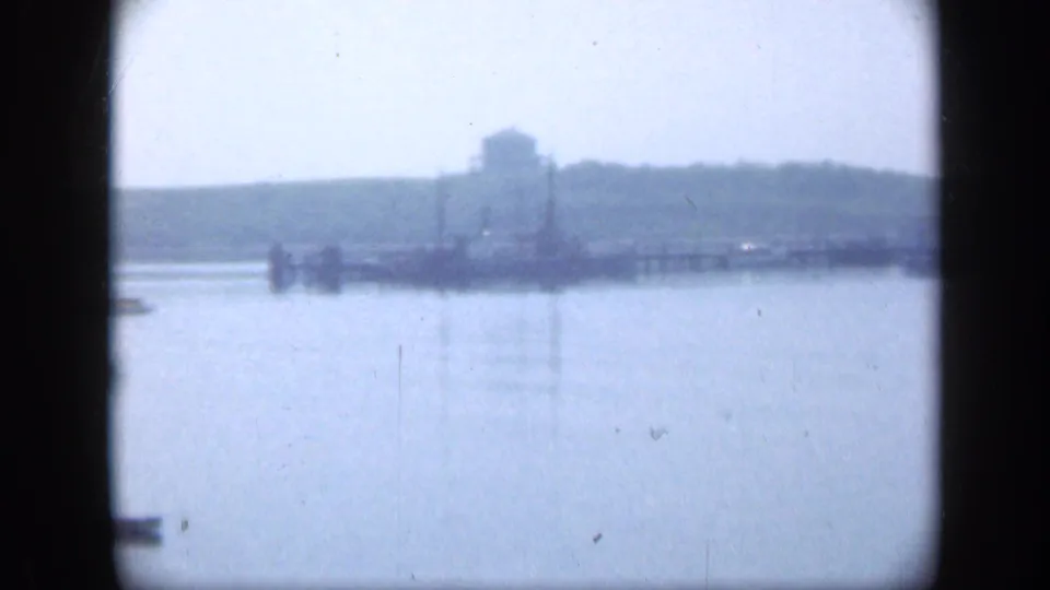 1948 Long Island 8mm frame showing a distant waterfront structure and low shoreline across calm water.