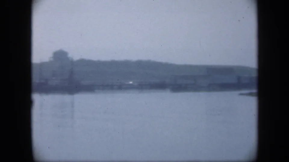 Soft 1948 Long Island waterfront view with open water in the foreground and a distant shoreline with a building-like form and poles.