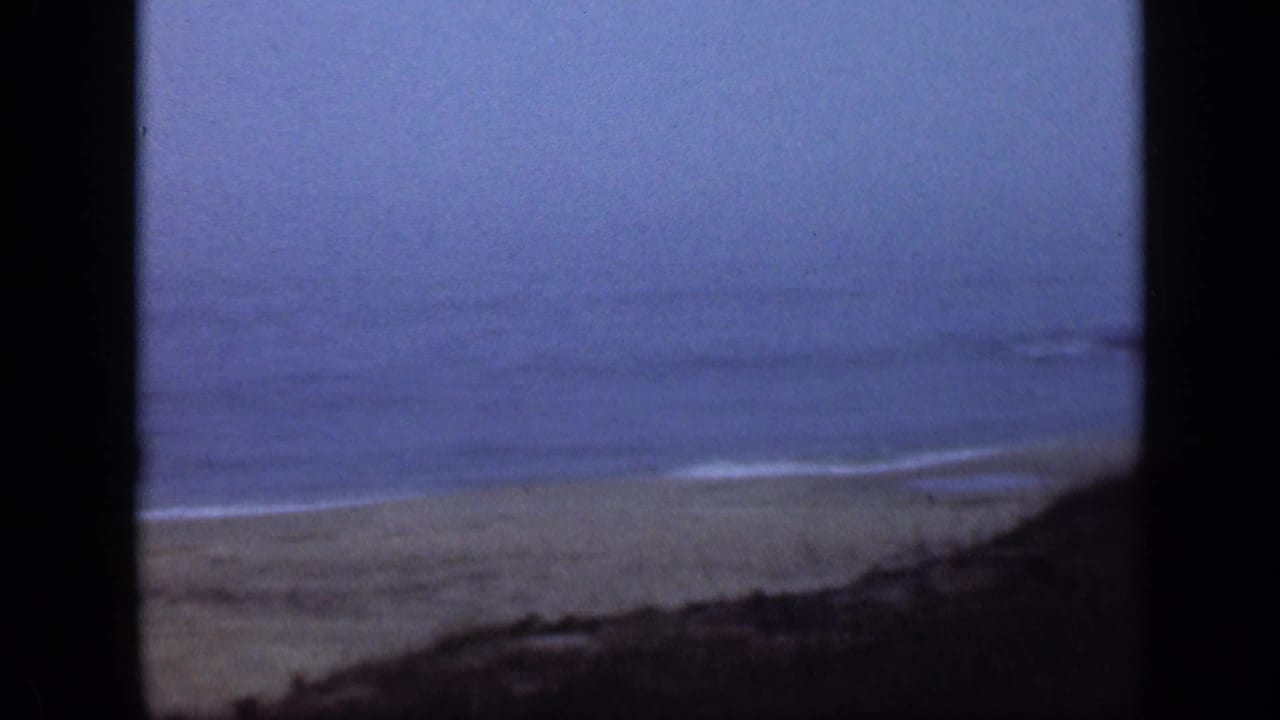 Sandy beach and gentle surf seen through dark vertical borders.