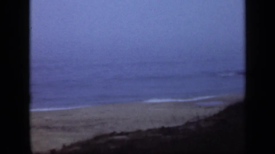 1948 Long Island beach view with pale sand, low waves, blue sky, and dark window-like framing at the edges.