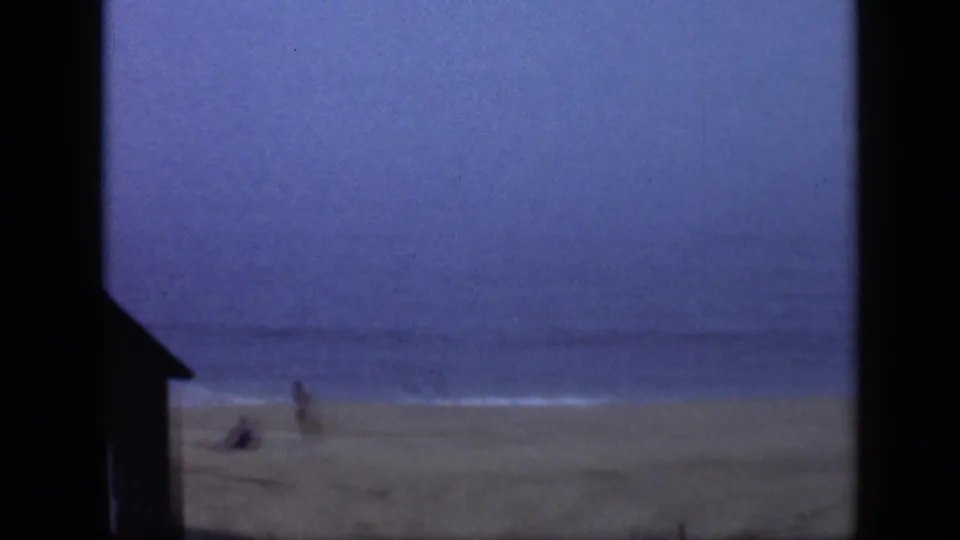 Long Island beach scene with a small distant person on the sand, low surf, blue sky, and dark framing along the left edge.
