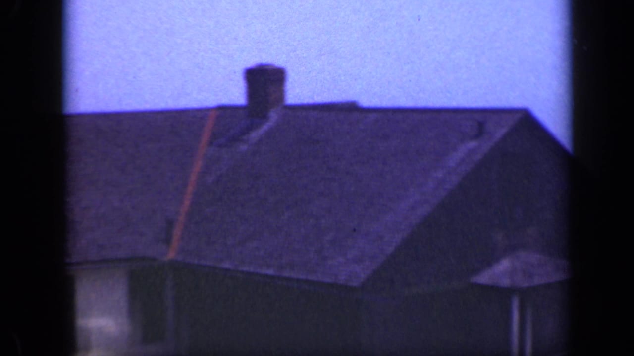 Dark shingled roof and chimney of a seaside house seen through film frame edges.