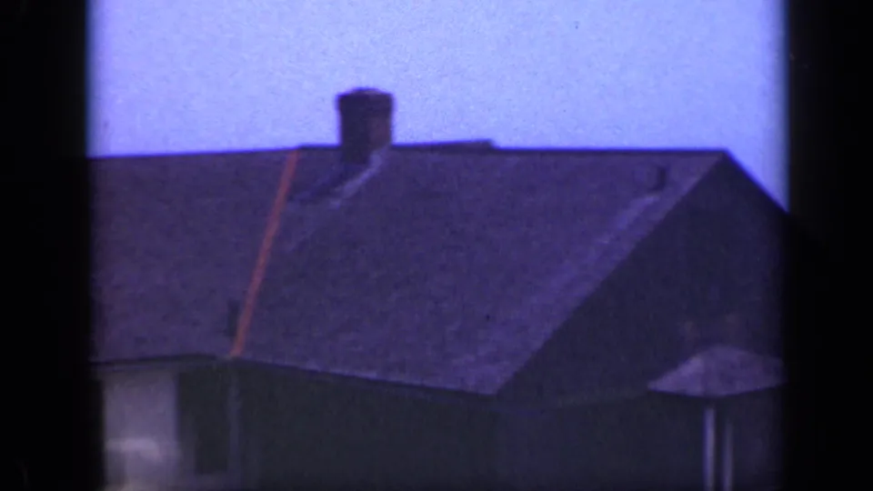 1948 Long Island home-movie frame showing a large beach house roof, chimney, and partial siding under a hazy sky.