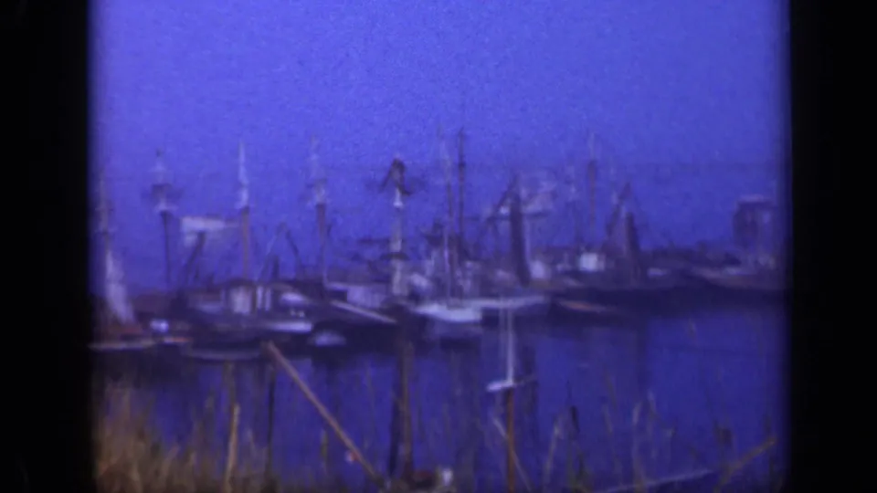 Blue-tinted 8mm frame of a Long Island marina in 1948, showing several old sailboats moored together with masts and harbor water.