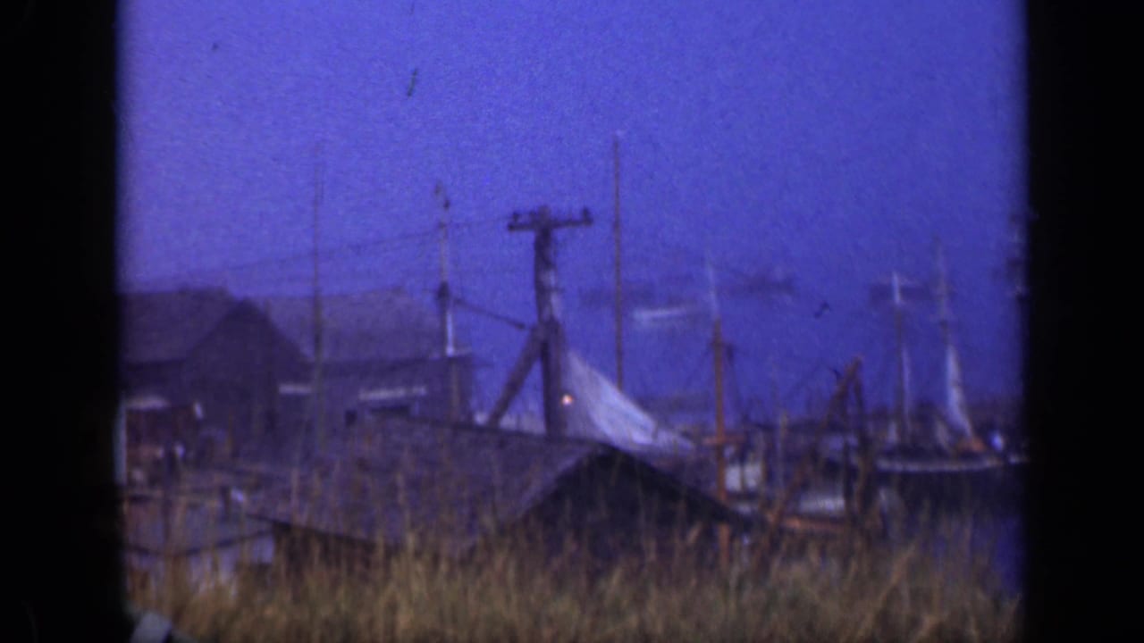 1948 Long Island waterfront view with utility poles, wires, dock structures, grasses, and low buildings under a blue dusk sky.