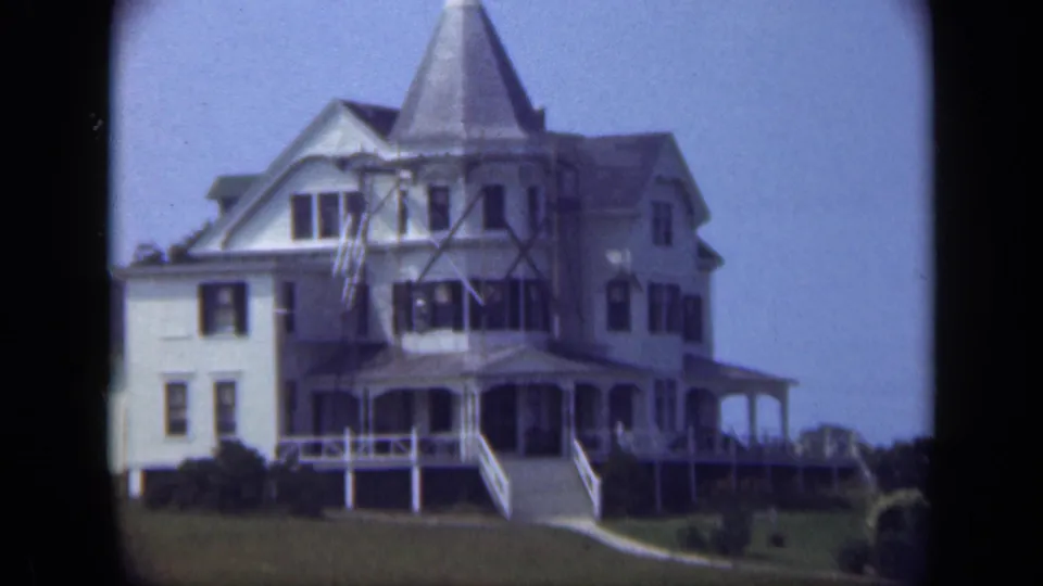 1948 Long Island view of a large white Victorian-style house with a turret, wraparound porch, steps, lawn, and shrubs.