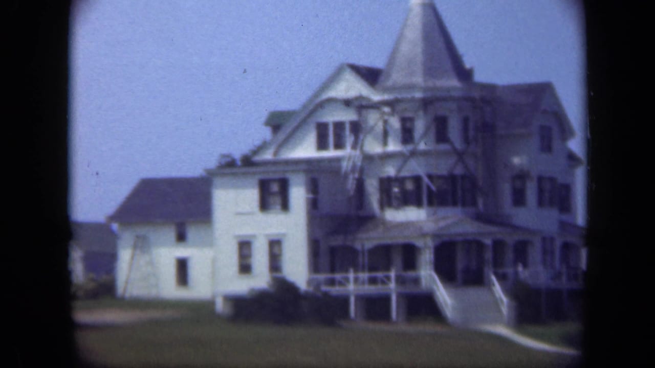 Large light-colored house with steep roof, porch, steps, and lawn.